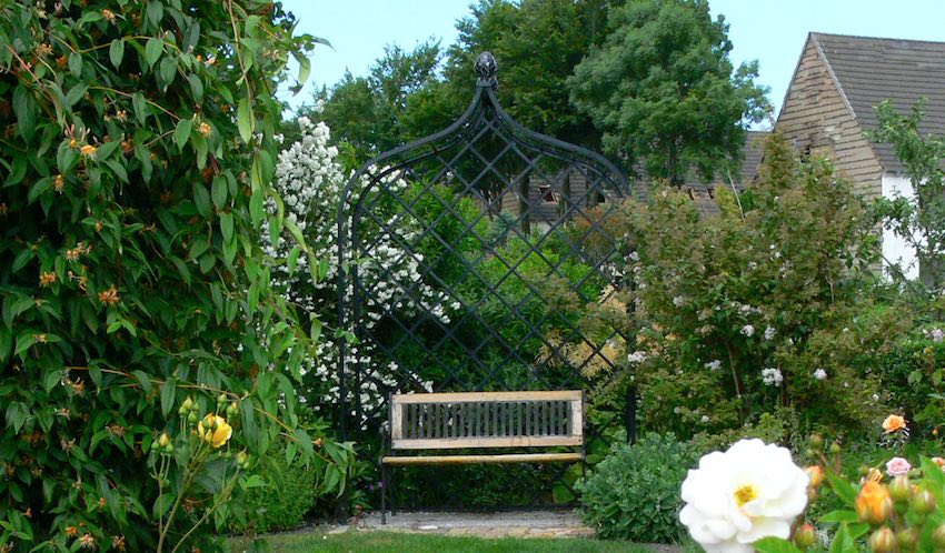 Unbewachsene Rosenlaube aus Metall mit Bank im Grünen