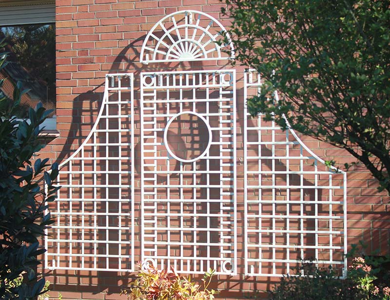 Gitterspalier aus Metall in weiss vor Klinkerwand