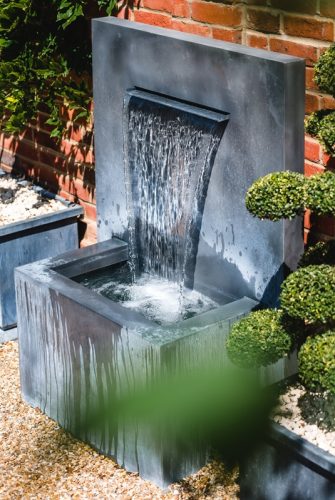 Arno Brunnen von A Place In The Garden plätschert im Hof von einer Ziegesteinwand im Detail Arno Brunnen von A Place In The Garden plätschert im Hof von einer Ziegesteinwand im Detail